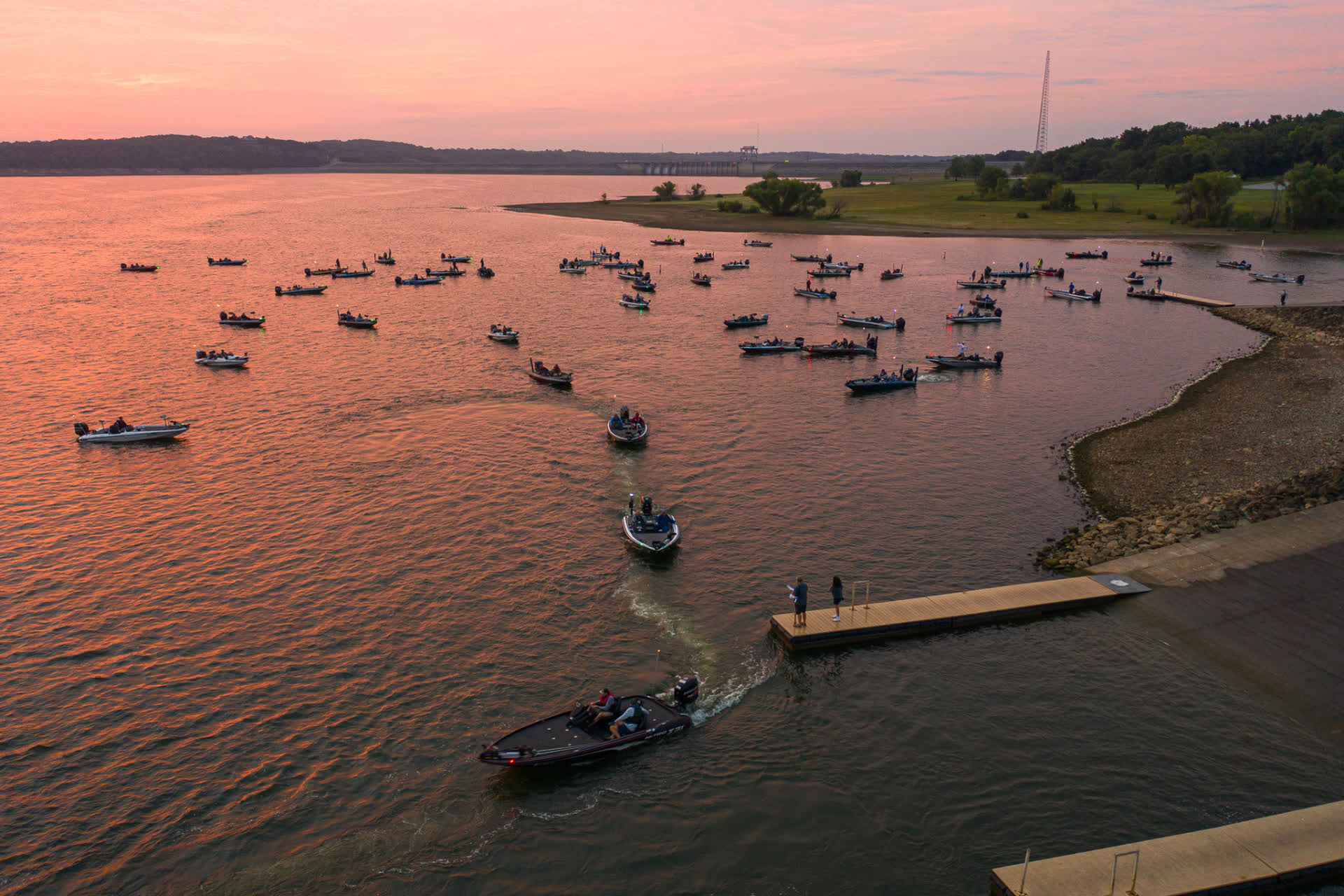 Dozens of bass boats staged near a Missouri lake ramp at sunset before takeoff